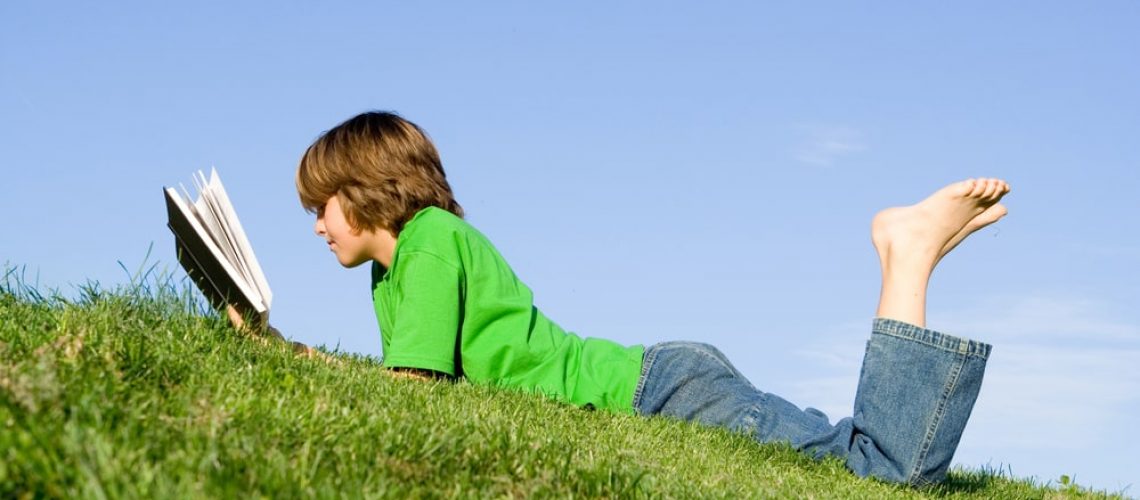 Boy Reading Outside In The Grass